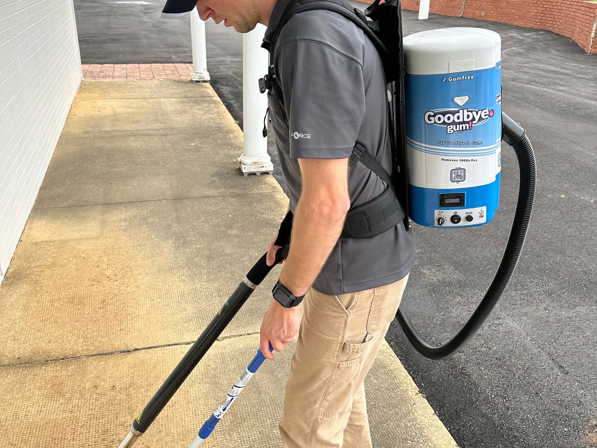 A person uses a backpack device to remove gum from pavement.